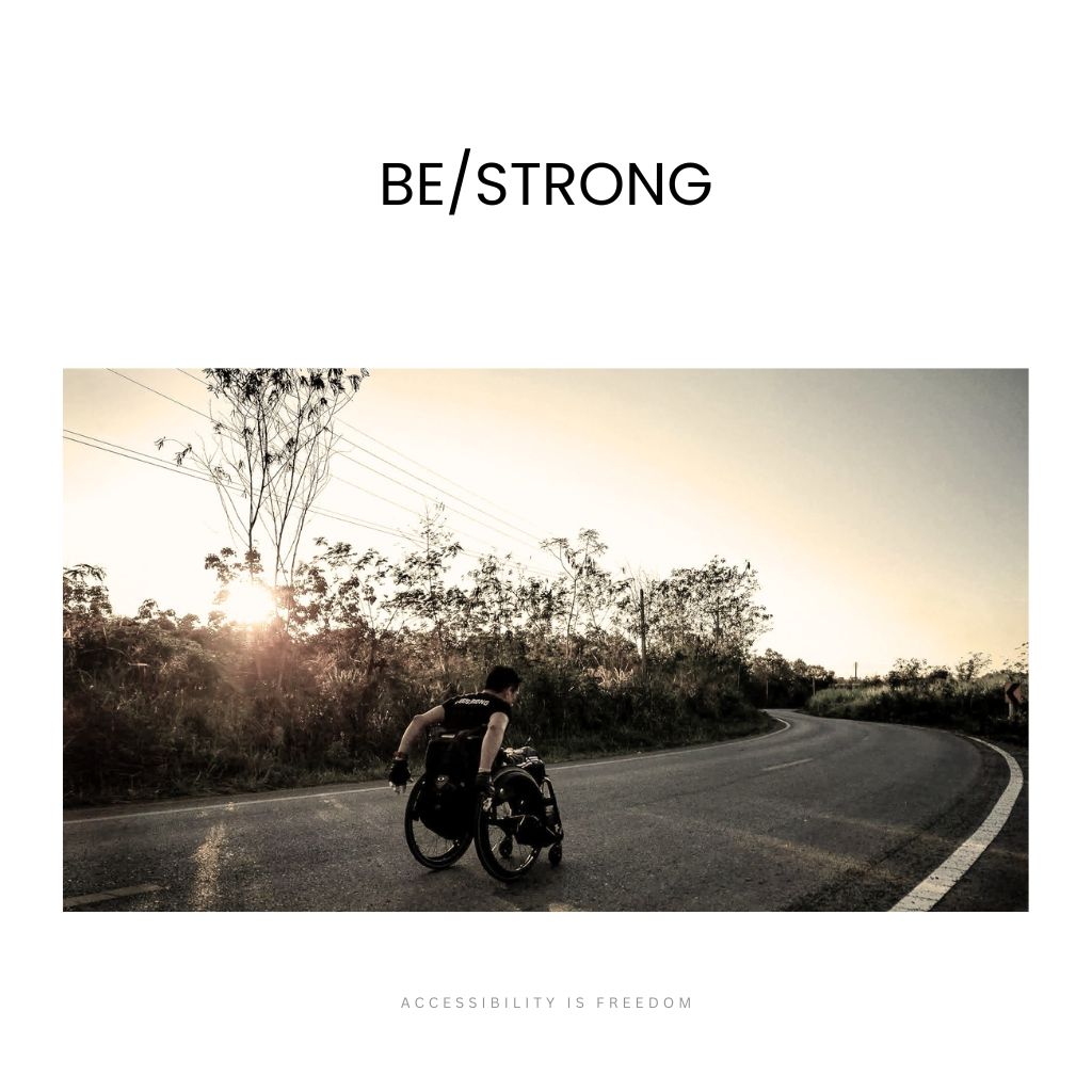 Wheelchair athlete pushing forward on a quiet country road into golden sunrise light, determined and strong; "BE/STRONG" headline above, "ACCESSIBILITY IS FREEDOM" tagline below.